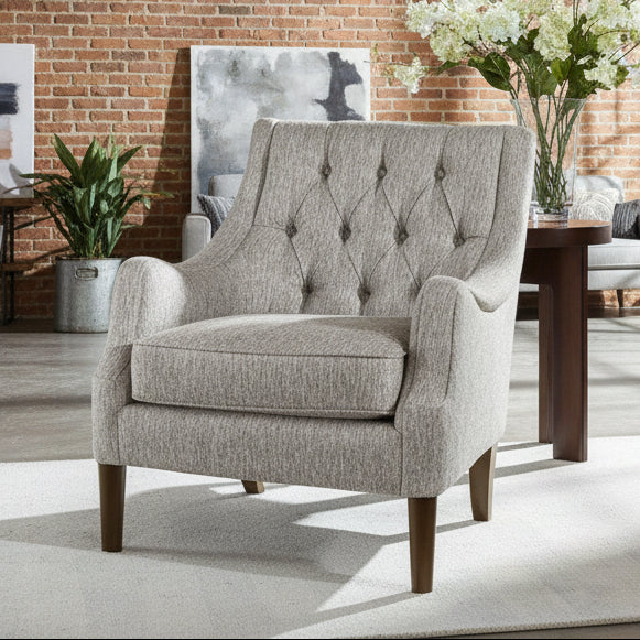 Gray upholstered armchair in a room with a window and a small table with flowers.